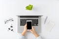 Overhead shot of female hands using smartphone with blank screen over laptop on white background. Office desktop. Royalty Free Stock Photo