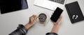 Female worker take a break with smartphone and hot coffee on modern worktable with office supplies