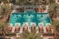 An overhead shot of a poolside lounge area with palm trees, cabanas, and people relaxing in stylish swimsuits, evoking the