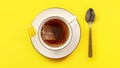 Overhead shot - porcelain cup with hot water, teabag just put in, staining the liquid, silver spoon next to it on yellow board Royalty Free Stock Photo