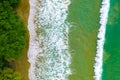 Overhead shot of a small wave on the shore leading to the green forest during daylight Royalty Free Stock Photo