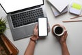 Overhead shot view of woman hand holding coffee cup and using smart phone at her office desk with laptop. Royalty Free Stock Photo