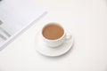 Overhead shot of a white cup filled with coffee on a saucer resting a white table