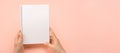 Overhead shot of woman hands holding blank notebook on pink table. Woman hands with mockup empty notepad on pastel background.