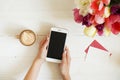 Overhead shot of woman hands holding cell phone gadget & coffee cup w cappuccino latte art on white wooden table background. Beaut Royalty Free Stock Photo