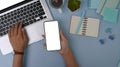 Overhead shot of woman holding mobile phone and working on laptop computer on pastel blue background. Royalty Free Stock Photo