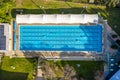 Overhead top down aerial shot of an outdoor olympic size, six lane, swimming pool in afternoon light, with people swimming laps