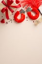 Overhead vertical shot of sensual accessories: playful handcuffs, feather tickler, gift box, candy, confetti on beige backdrop