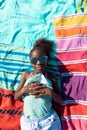 Overhead view of african american girl wearing sunglasses and lying on towels at beach