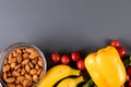 Overhead view of almonds in bowl with banana, cherry tomatoes and yellow bell pepper on table