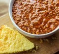 Close up view of a bowl of authentic chili, shown with a crumbly piece of buttermilk cornbread.