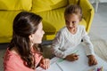 View of cheerful babysitter looking at cute kid in living room