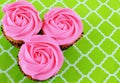 Overhead view of 3 cupcakes with rose shaped pink frosting