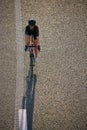 Overhead view of female cyclist riding alone on empty textured highway, casting long shadow along dashed lane marking. Royalty Free Stock Photo