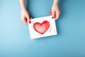 Female hands holding card with heart on blue background.