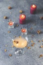 Overhead view of grapefruit martini cocktail with dried roses flowers and petals, surrounded candles on dark gray table surface