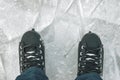 An overhead view of the legs in black skate boots against the background of the ice rink.