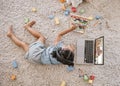 Overhead view of a little cute girl using a laptop and wireless headphones while laying on the floor in the lounge Royalty Free Stock Photo