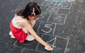 Overhead view of a little girl drawing with chalk hopscotch on playground. Child playing the game outside. The kid draws hopscotch