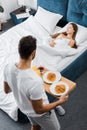 Overhead view of man holding wooden tray with breakfast while woman sleeping Royalty Free Stock Photo