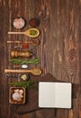 Overhead view of open cookbook for recipes laying next to kitchen spoons and bowls with spices and seasonings