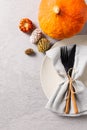 Overhead view of plate with cutlery and napkin, pumpkin, pine cones and copy space on grey