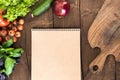 Overhead view of raw vegetables, chopping board and blank notepad on wooden table Royalty Free Stock Photo
