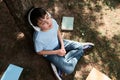 Relaxed teenage boy listens to music on headphones, sitting on the grass near copybooks scattered on the grass in a park Royalty Free Stock Photo