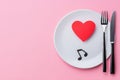 An overhead view of a table set with a plate, silver fork and knife, and a paper heart adorned with music notes. Royalty Free Stock Photo