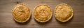 Overhead View of three Cooked Round Meat Pies on Wooden Countertop