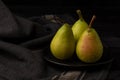Overhead view of three green pears with water drops in black plate on dark table
