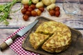 Almost overhead view of a typical Spanish potato omelette with a separate portion with potatoes and cherrie tomatoes in a rustic Royalty Free Stock Photo