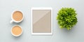 Overhead view of a white tablet two coffee cups and a green leafy plant on a light blue surface Royalty Free Stock Photo