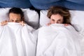 overhead view of wife and husband hiding under blanket while lying in bed