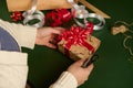 Overhead view of woman& x27;s hands tying beautiful bow from a shiny red ribbon while decorating a Christmas gift