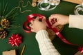 Overhead view of woman's hands tying up a christmas present with a decorative shiny red ribbon over a green