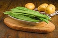 Wooden board with an array of fresh green beans and potatoes placed on the side