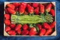 Overhead view of a wooden tray with a bunch of green wild asparagus surrounded by fresh strawberries. Royalty Free Stock Photo