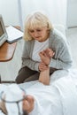 View of worried senior woman sitting near ill husbend and holding his hand in hospital