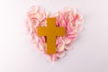 Overhead of yellow christian cross on heart shape of pink rose petals, on white background Royalty Free Stock Photo