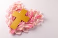 Overhead of yellow christian cross on heart shape of pink rose petals, on white with copy space Royalty Free Stock Photo