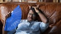 Overheated afro american man recline on couch use hand fan Royalty Free Stock Photo