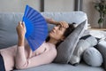 Overheated young woman relax on sofa wave with hand fan
