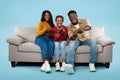 Overjoyed african american parents and their daughter playing video games, sitting on sofa over blue background Royalty Free Stock Photo