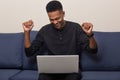 Overjoyed Afro American woman raises hands in fists, smiles gladfully as sees electronic results of exam, feels triumph, dressed Royalty Free Stock Photo