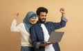 Overjoyed arab couple holding laptop and celebrating success with clenched fists Royalty Free Stock Photo