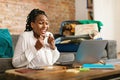 Overjoyed black lady rejoicing to travel and win, making success gesture, sitting in front of laptop in living room Royalty Free Stock Photo