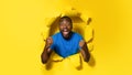 Overjoyed black man shouting happily, clenching both fists, cheering great success, posing in ripped yellow paper hole Royalty Free Stock Photo