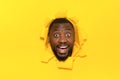 Overjoyed black man standing through torn hole of yellow background, looking surprisingly at camera Royalty Free Stock Photo