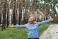 Overjoyed blonde woman in blue raincoat enjoying silence natural green environment woods in the forest. Happy emotion Royalty Free Stock Photo